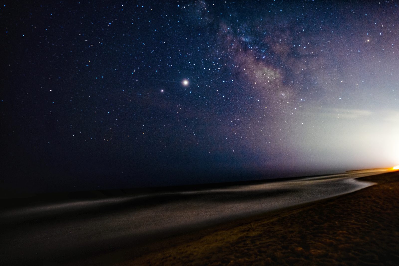 The Milky Way stretches across a starlit sky above a serene beach at twilight.