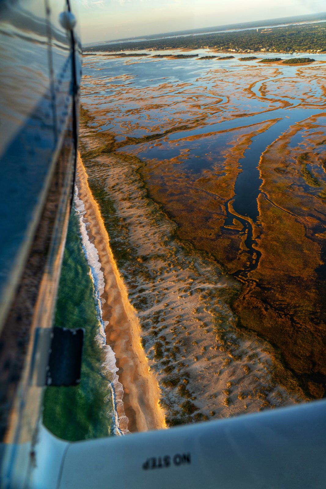 Aerial view from a small aircraft showing a coastal wetland with winding waterways and golden marshland.
