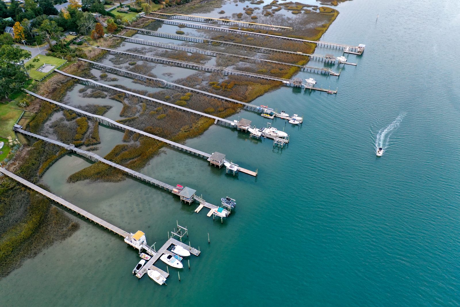 Aerial view of a coastal marina with multiple docks, moored boats, and salt marshes along the waterfront.